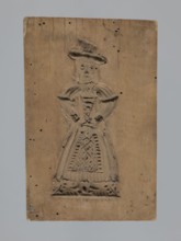 Double-sided gingerbread form. Obverse: female figure in a long patterned dress wearing a hat.