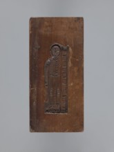 Double-sided gingerbread form. Side A: female figure with a scarf on her head, standing, leaning on