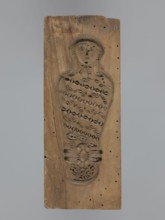Double-sided gingerbread form. Obverse: female figure in a hat and a long patterned dress. Reverse: