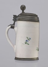 Cylindrical tankard in a pewter frame. White faience painted in colors. From the front, a barefoot