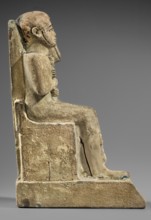 Figurine of the god Ptah sitting on a throne, on a base in the shape of the sign of Maat. He holds