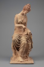 Figurine of a woman sitting on a rock with a flower in her hand. Woman sitting on a rock with a