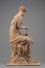 Figurine of a woman sitting on a rock with a flower in her hand. Woman sitting on a rock with a
