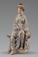 Figurine of a woman. A girl sitting in a chair is dressed in a soft white chiton over which a blue,