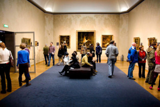 Room with paintings and visitors, three still lifes hang at the back with dead animals; Exhibition Damien Hirst - For Th