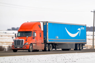 Banff, Alberta, Kanada. 2. April 2025. Ein orangefarbener Amazon Prime-Sattelschlepper fährt auf einer verschneiten Straße durch eine ländliche Landschaft mit einem Strommast im Hintergrund.