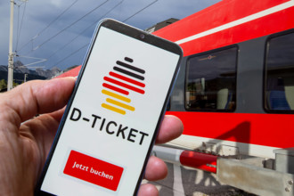 (Fotomontage) Logo vom Deutschlandticket auf dem Smartphone vor einem vorbeifahrenden Nahverkehrszug *** Photomontage lo