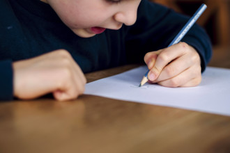 Symbolfoto zum Thema Linkshaender: Ein fuenfjaehriger Junge sitzt zu Hause und schreibt mit einem Bleistift in der linke