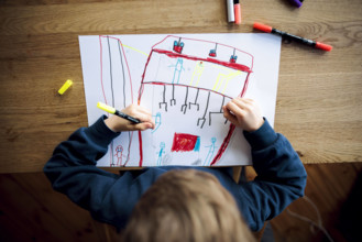 Symbolfoto zum Thema Kreativitaet bei kleinen Kindern: Ein fuenfjaehriger Junge sitzt zu Hause und malt mit Buntstiften