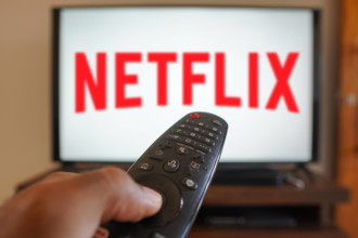 April 20, 2024, Brazil. In this photo illustration, a hand holding a TV remote control in front of the Netflix logo on a