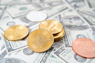 Germany - November 6, 2024: Bitcoin gold coins on US dollar banknotes. Symbolic image for the importance of cryptocurren