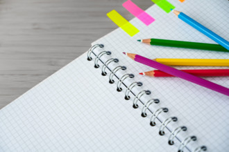Buntstifte auf einem Teil eines Spiralheftes und bunte Marker auf einem grauen Schreibtisch, kreatives Arbeiten oder Schulmaterial, Kopierraum, ausgewählter Fokus