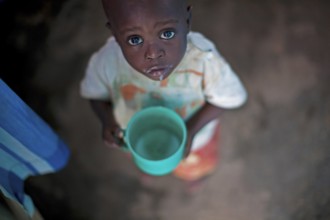kleiner Junge mit Plastikbecher und schaut mit grossen Augen hoch in die Kamera, Burundi, Bujumbura little boy with pla