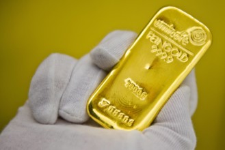 Eine Hand mit Handschuh haelt einen Goldbarren im Tresor des Goldhandels Pro Aurum Muenchen 16 02 2