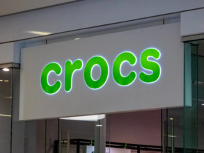 Edmonton, Alberta, Kanada. 24. Mai 2025. Das markante, grün beleuchtete Crocs-Logoschild signalisiert die Präsenz der beliebten Schuhmarke und zieht mit seinem verspielten Design die Aufmerksamkeit au...