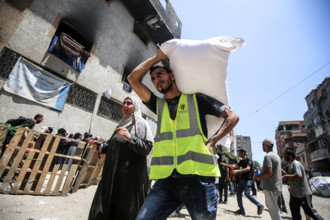 Palestinians carry away bags of flour as others wait in front of a distribution point set up by the United Nations World Food Programme