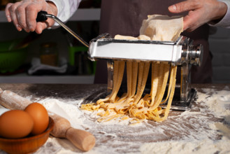 Kaukasische weibliche Hände bei der Herstellung von Fettuccine-Nudeln mit einer mechanischen Nudelmaschine
