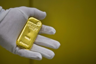 Eine Hand mit Handschuh haelt einen Goldbarren im Tresor des Goldhandels Pro Aurum Muenchen 16 02 2