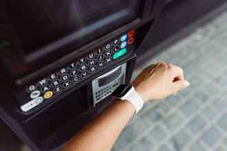 Person, die mit einer Smartwatch kontaktlos bezahlt, um einen Parkplatz zu bezahlen. Bezahlen am Parkautomaten. Ein Kunde bezahlt sein Parkticket schnell und einfach kontaktlos mit einer Smartwatch. V...