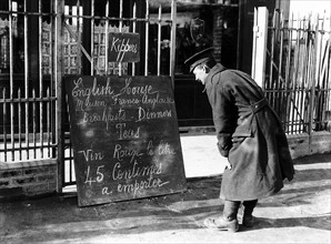 British soldier reads a menu outside a restaurant in France, with red wine at 45 centimes a litre.