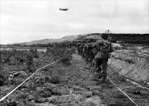 American infantrymen move along a taped path through a German minefield after their beach landing