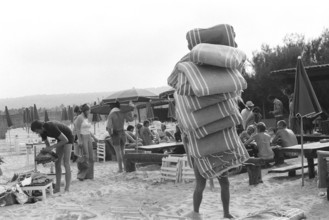 Saint-Tropez, France, 17th June 1975, man carrying Sun Lounger Cushions.