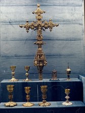 Display case containing chalices and a gold processional cross