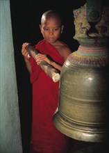 Un jeune moine sonne la cloche pour le temps de la prière, au temple de Myanmar