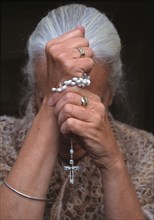A Roman Catholic woman holding as rosary as she prays