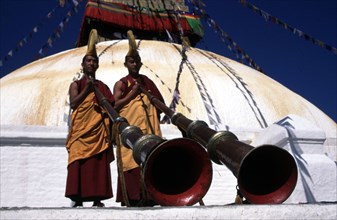 Two monks blowing horns during Tibetan New Year 'Losar', at Bodnath Stupa, Nepal