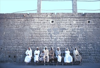 Arab men and a girl sitting on a street bench in Ajman during the fast month of Ramadan