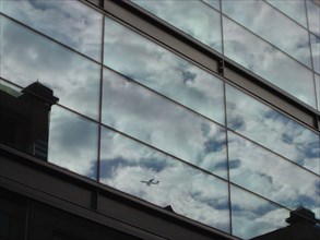 Reflection of clouds and plane in a building of the City in London