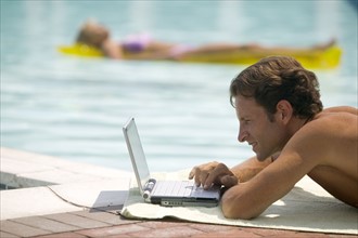 A man poolside using a laptop computer.