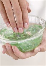 Female fingers in a dish of aloe gel.