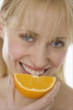 Smiling woman eating orange slice.