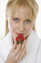 Woman in bathrobe eating strawberry.