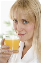 Woman in bathrobe drinking orange juice.