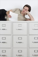 Man reading lying atop file cabinets.