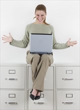 Woman with laptop atop file cabinets.