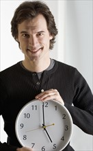 Smiling man holding clock.