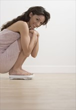 Smiling woman crouching on bathroom scale.