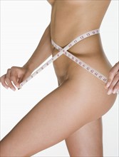 Nude female measuring her waist.
