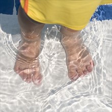 Child's feet standing in water.