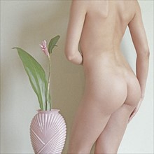 Nude female posing with flower in vase.