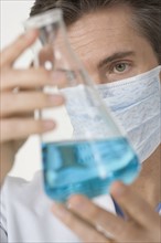 Masked scientist examining blue liquid.