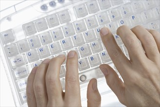 Closeup of hands on transparent keyboard.