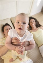 Infant held up by smiling couple.