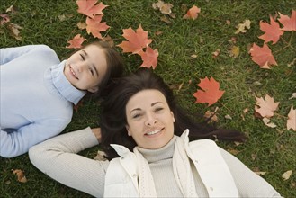 Mother and daughter lying on grass on fall day.