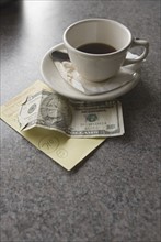 Sill life of cup of coffee money and check.