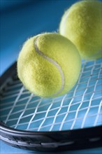 Closeup of tennis racquet and two balls.